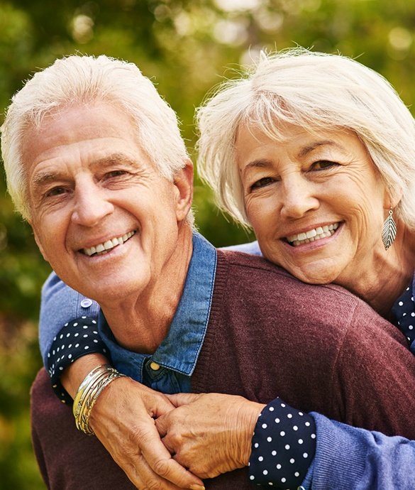 Older man and woman smiling together after dental implant tooth replacement