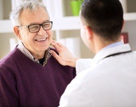 Older man smiling and shaking hands with periodontist