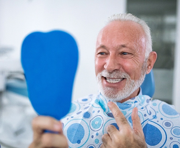 Older periodontal patient smiling in dental mirror