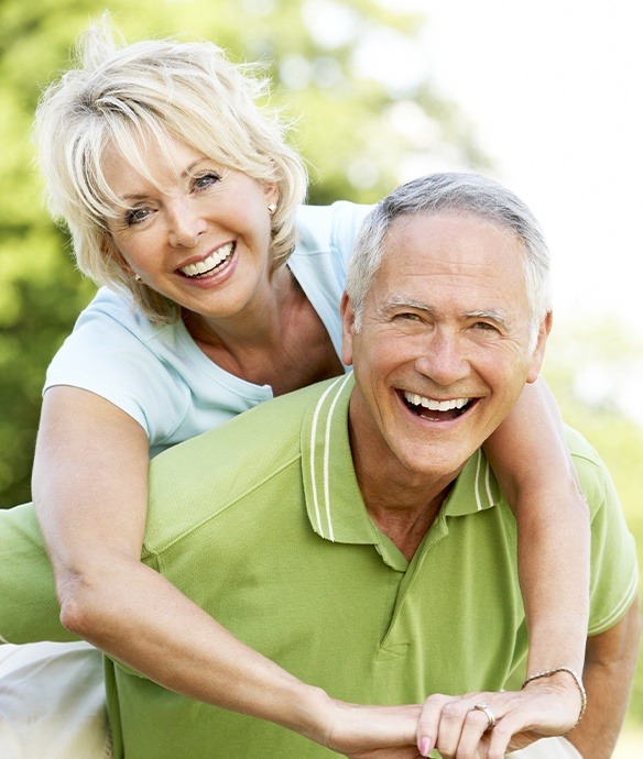 Older man and woman smiling after hybridge dental implant restoration