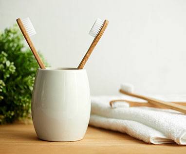 Toothbrushes in cup on wooden table next to towel