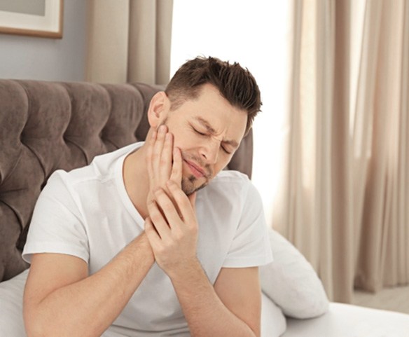 Man sitting in bed rubbing jaw in concern