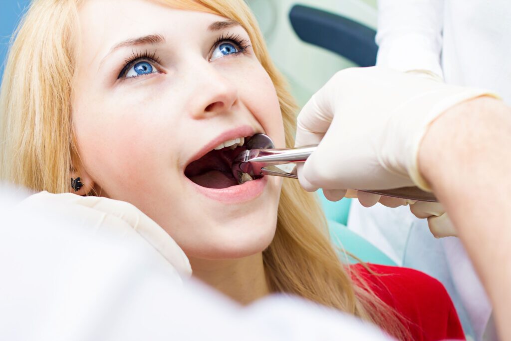 Dentist in white gloves extracting woman's tooth